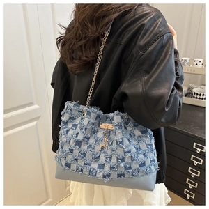 Detail of plaid denim tote bag with frayed fringe textures and gold deer pendant charm