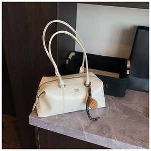 Detail of cream leather bowling bag featuring metal logo and decorative woven keychain