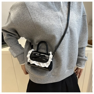 Close-up of black leather square bag featuring a delicate white lace trim and bow detail