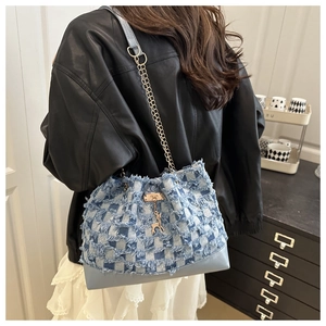 Détail du sac seau en denim damier bleu avec bords effilochés et breloque cerf doré