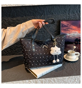 Close-up of black tote bag featuring textured fabric and decorative golden bow detail