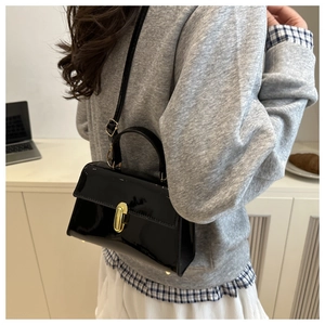 Detail of a chic black patent leather crossbody bag with a gold buckle worn by a model