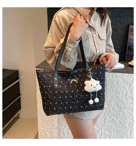 Detailed close-up of a black pleated tote bag with bow hardware and plush cloud charm
