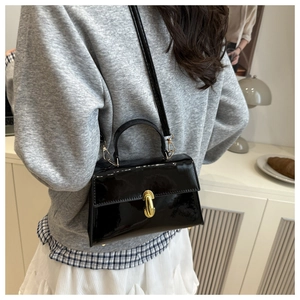 Detail of minimalist black patent leather crossbody bag with golden U-shaped metal buckle