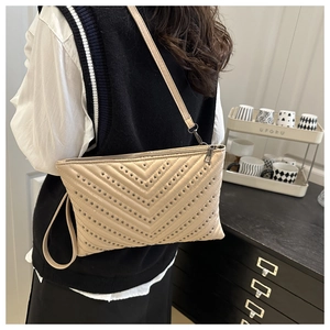 Detail of beige crossbody bag featuring V-shaped quilting and dark metal rivet studs