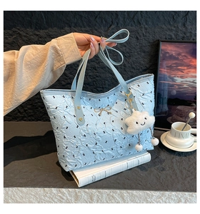 Close-up of light blue quilted tote bag with golden bow and cloud plush charm