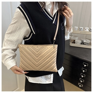Detail of beige V-quilted envelope bag with dark metal rivets on a stylish shoulder strap