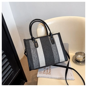 Detail of striped canvas tote bag featuring premium black handles and gold hardware