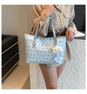 Detail of light blue quilted tote bag with gold bow accent and cloud charm on shoulder