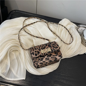 Mini leopard print crossbody bag with gold twist lock and chain strap on white fabric