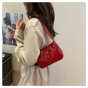 Detail of red glossy patent leather shoulder bag with drawstring and golden eyelets