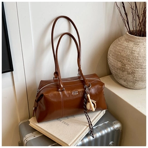Detail of dark brown glossy leather bowling bag with silver logo and baseball charm