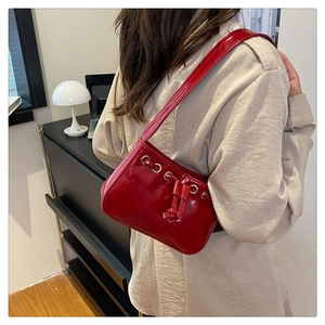 Detail of red glossy patent leather handbag with gold eyelets and drawstring accents