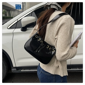 Detail of glossy black faux leather shoulder bag with gold eyelets and drawstring tie