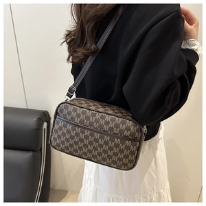 Detail of a dark brown crossbody bag with M-pattern and adjustable silver metal buckle