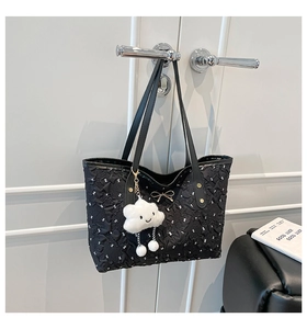 Detail of black pleated tote bag featuring golden bow and plush cloud pendant