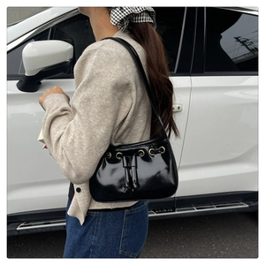 Detail of black glossy patent leather shoulder bag with gold metal eyelets and drawstring