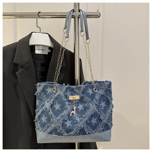 Detail of blue denim tote bag featuring star patterns and distressed fringe edges