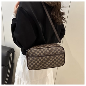 Detail of a deep brown crossbody camera bag with M-pattern monogram and silver zipper
