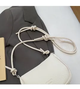 Detail view of cream white textured crossbody bag with decorative rope knots on strap