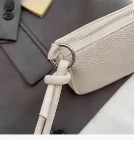 Detail of white lychee leather handbag with silver ring zipper and knotted strap handle