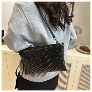 Detail of black quilted envelope bag featuring V-shaped metal studs and silver chain strap