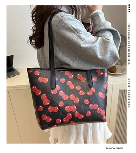 Fashionable black tote bag with red cherry print being worn as an underarm shoulder bag