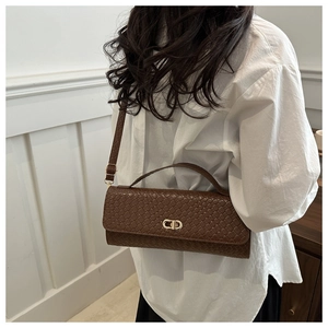 Detail of a brown woven texture handbag featuring a gold metallic buckle on a model