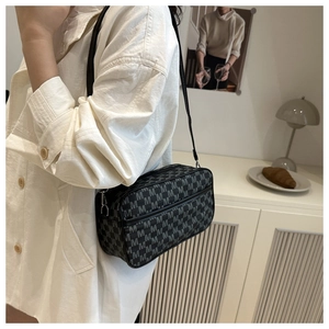 Close-up of black crossbody bag with white M-letter print shown on a model