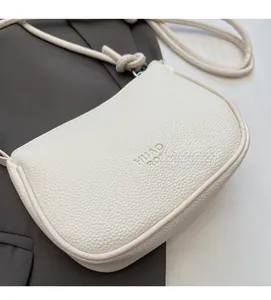 Detail of white pebble grain leather crossbody bag with brand embossing and knotted strap