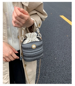 Détail d'un sac seau tissé avec ornement de perle et poignée en chaîne blanche