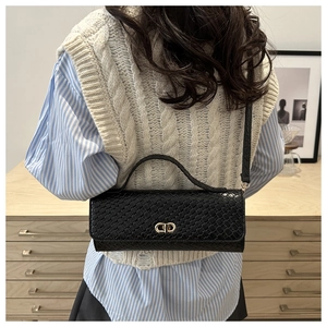 Detailed view of black woven shoulder bag with gold CD clasp on casual knit outfit