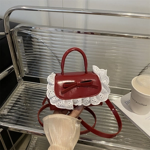 Mini red crossbody bag with sweet bow and white lace trim on a stylish silver chair
