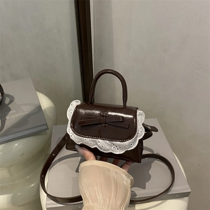 Mini brown leather crossbody bag with white lace trim and bow detail held by hand