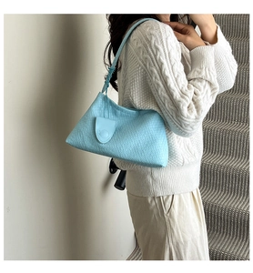 Detail of light blue woven shoulder bag with small heart charm on leather strap