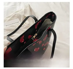 Close-up of smooth gold metal zipper and red cherry print on black leather tote bag