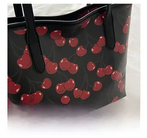 Close-up of black tote bag featuring a vibrant red cherry pattern on smooth leather
