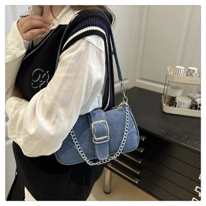 Detail of blue denim shoulder bag with silver metal buckle and chain strap on model