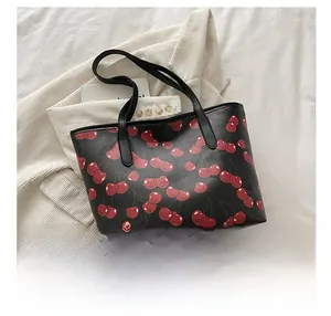 Detail view of large tote bag featuring vibrant red cherry prints on black leather material