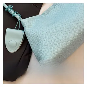 Detailed view of light blue woven leather texture and matching tag on the shoulder bag