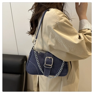 Close-up of denim shoulder bag with white contrast stitching and silver metal chain strap