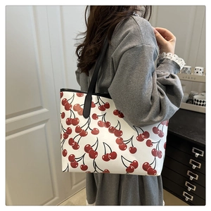 Detail of white tote bag with cherry print and black strap on a grey sweater