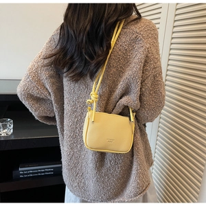 Detail of a bright yellow mini crossbody bag with lychee texture and knotted strap design