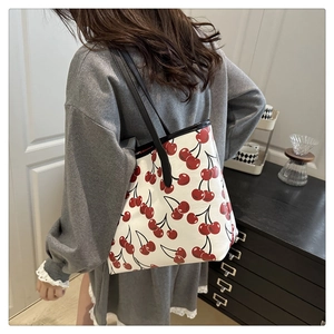 Close-up of a stylish white tote bag with red cherry prints and black shoulder straps