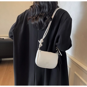 Detailed close-up of white lychee leather saddle bag with shoulder strap and embossed logo