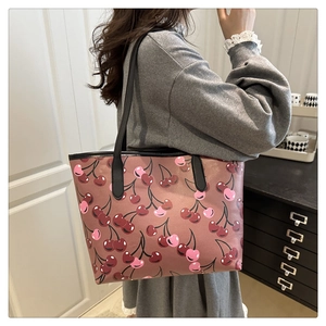 Detail of a large cherry print tote bag worn over the shoulder on a grey sweater
