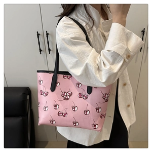 Detail of pink cherry print tote bag with black leather straps on a female shoulder