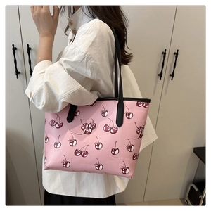 Detail of pink cherry print tote bag with black contrast trim on a model's shoulder