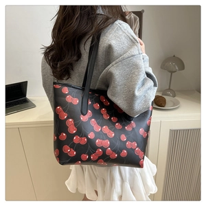 Detail of black tote bag featuring vibrant red cherry prints and slim shoulder straps