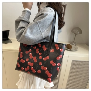 Detail of a black leather tote bag with red cherry prints shown on a model's shoulder
